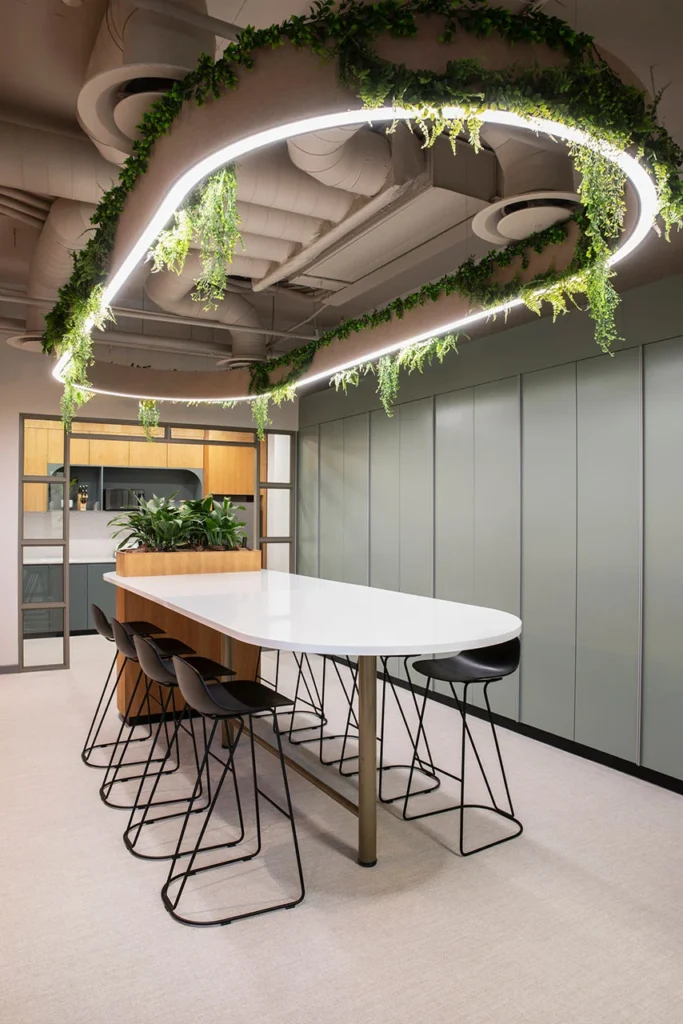 Canteen with seating and curved linear pendant lighting with integrated greenery in European Investment Bank office in Johannesburg