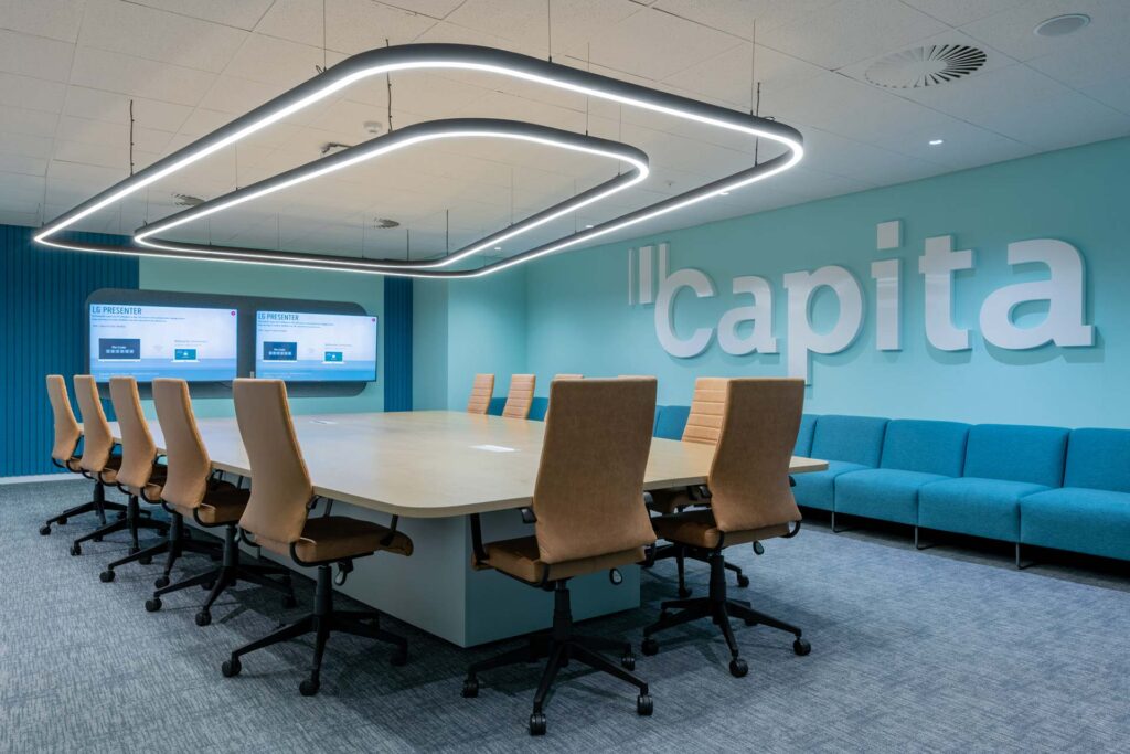 Large boardroom table with tan leather office chairs and halo lighting as well as booth seating against the wall with a large capita branding sign