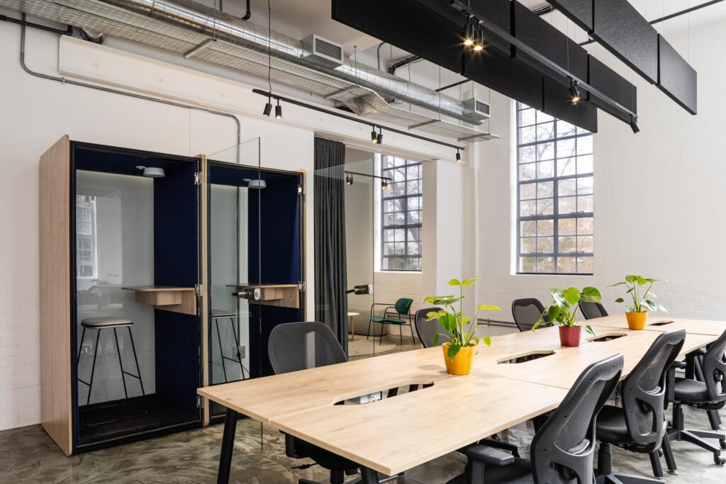Acoustic meeting booths alongside open plan tables and task chairs for collaborative workplace furniture solutions
