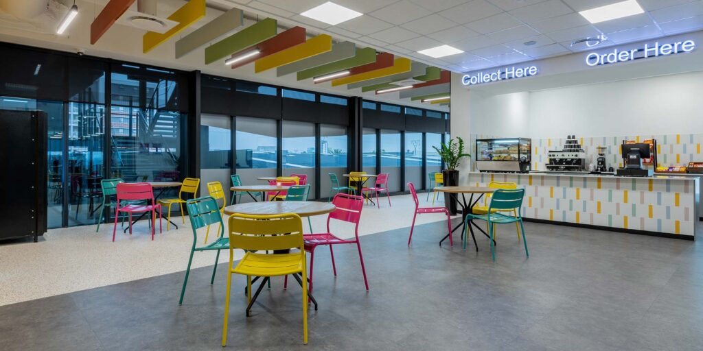 Call centre office canteen with green and yellow picnic-style chairs, round timber tables and contemporary FF&E furniture
