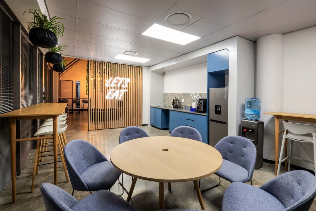 Mazars International office canteen area features LED signage, round wooden tables with comfortable seating, and bar stools.