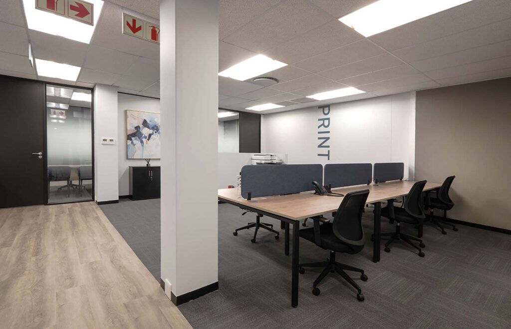 One Vision Pretoria office, featuring shared wooden desks, chairs, partition screens, and storage solutions.